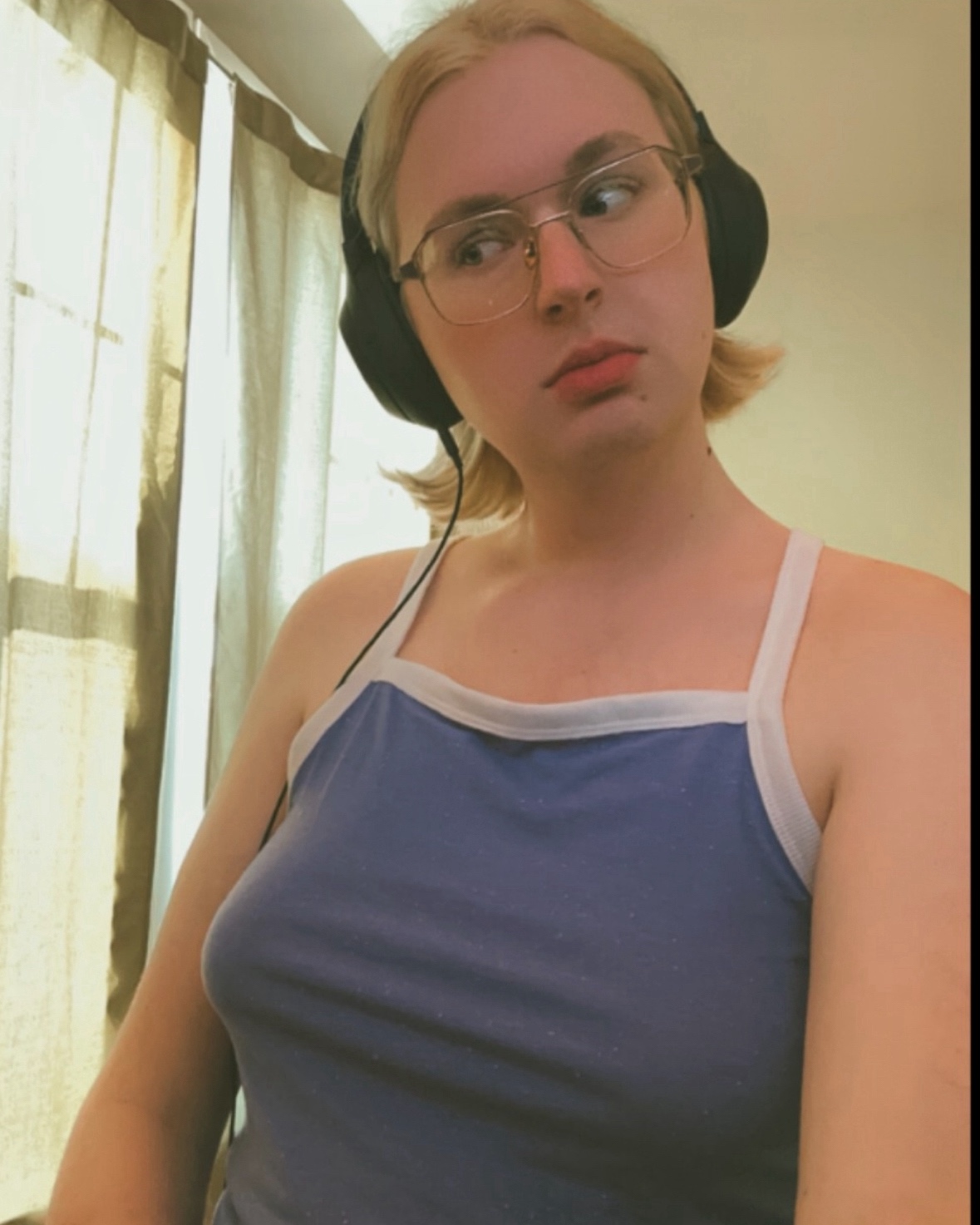 blonde woman in a pale blue tank top wearing wired over-ear headphones and looking to the side; selfie