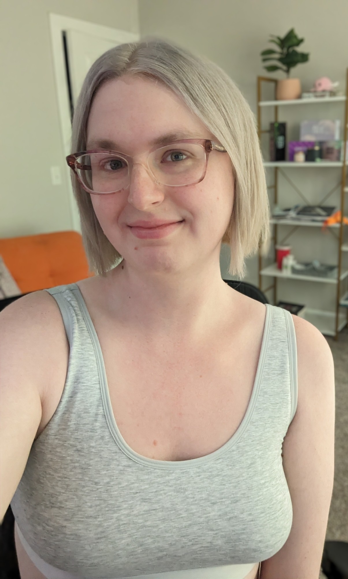 skylar, a blonde trans woman sitting in her office, smiling in a light gray sports bra.