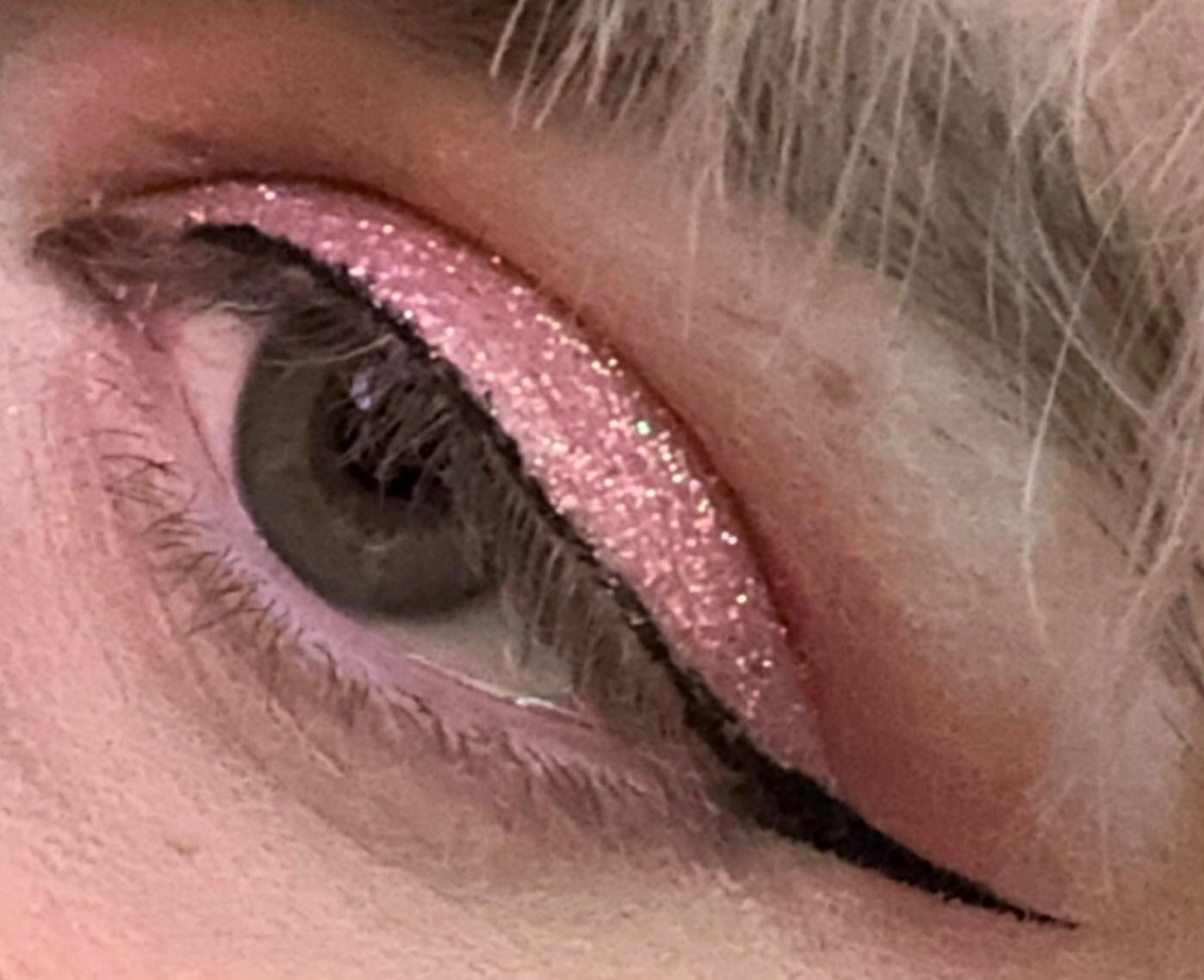 a close up photo of skylar’s eye, she has a rose glitter in her lid, a peach matte shadow blended out above the crease, and incredibly thin and sharp black winged eyeliner
