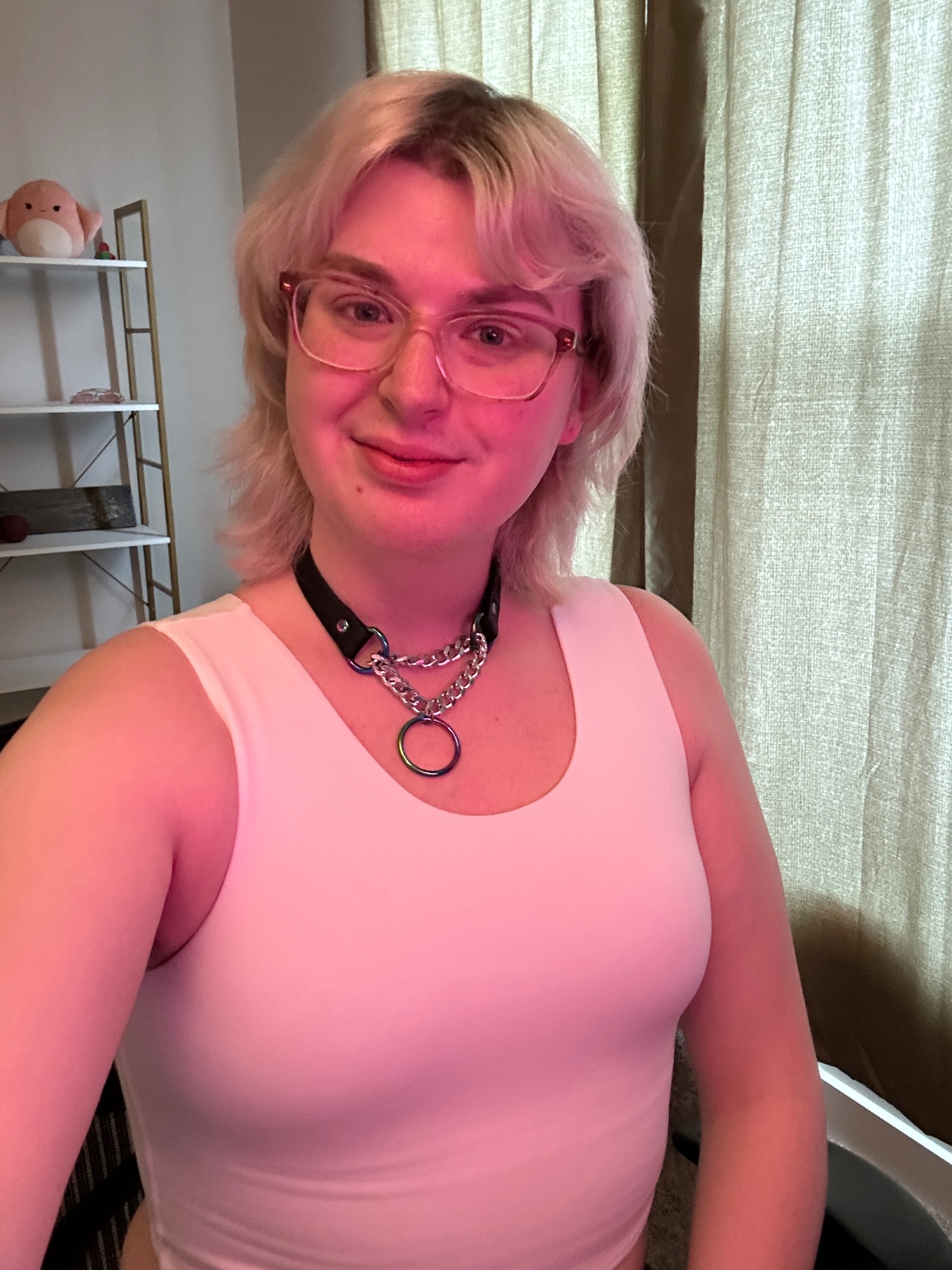 Ethan, sitting in his desk chair, wearing just a white binder tank top and a black leather martingale collar with silver chain and rainbow hardware. his breasts are noticeably compressed. he has pink 
