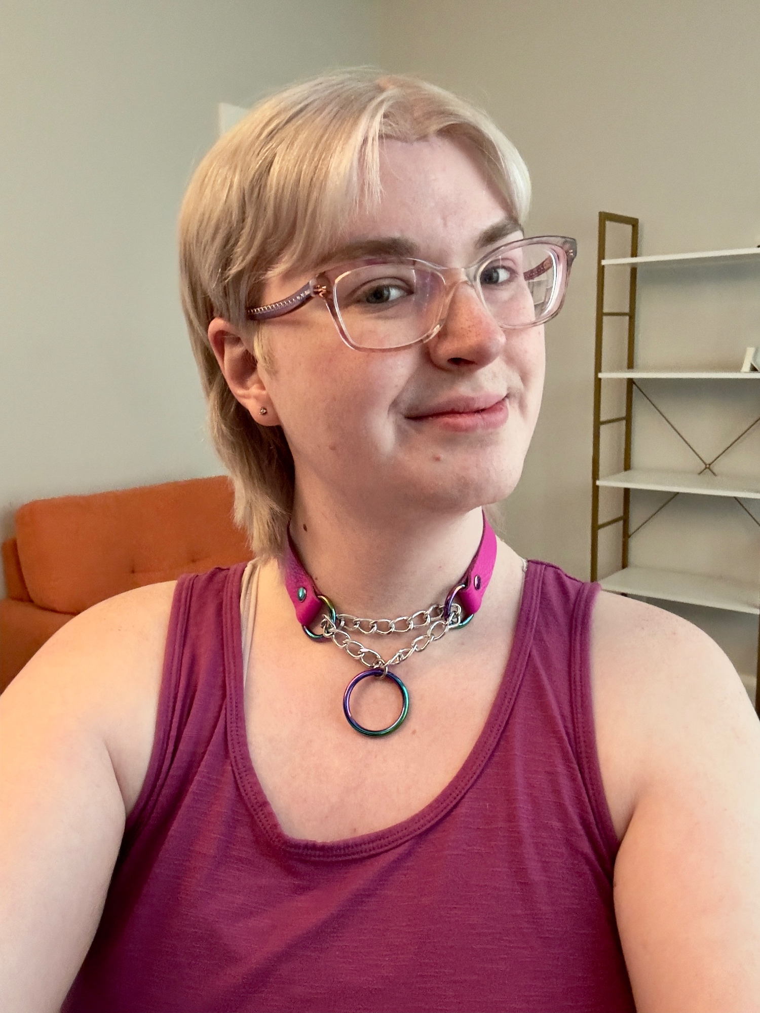 a selfie of zari, with their new hair which is platinum blonde with a middle part, cut short on the sides above the ears, and long in the back just above shoulder length. they're wearing a purple tank