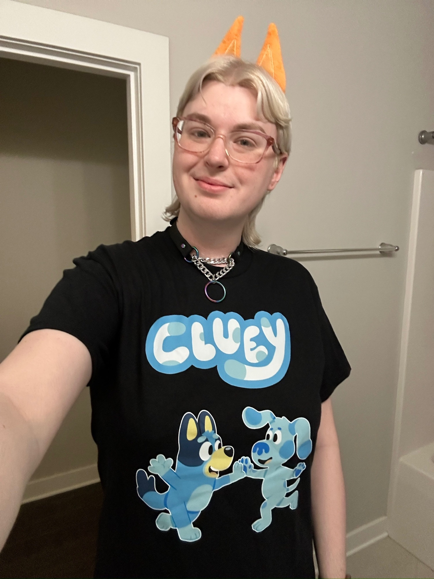 a selfie of zari, wearing a black shirt with a "Cluey" design, the text is white, and in the shape and font of the Bluey logo, but has light blue spots like Blue from Blue's Clues, and a slightly deep
