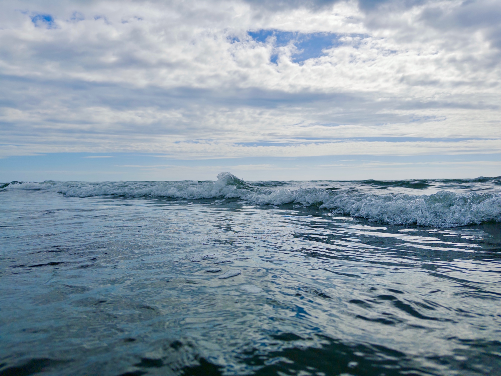 low-angle view of rippling blue water with a small wave breaking under a textured cloudy sky